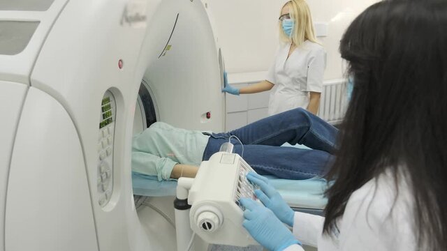 Two radiologists inserts an intravenous catheter to inject contrast to female patient who is undergoing CT or MRI scan. Patient lying on a CT or MRI scan bed, moving inside the machine.