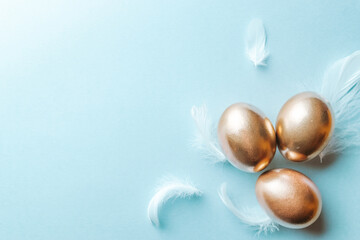 Obraz na płótnie Canvas Basket easter decoration: Golden eggs with white feathers on pastel blue background. Congratulatory easter design. Top view.