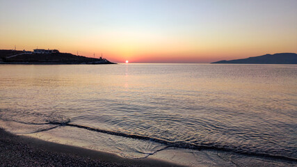 Orange sunrise sun shining on clear sky horizon on pebble beach coast near Athens in Greece. Summer travel calm sea shore in morning