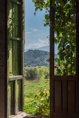 Views from inside an old house, through a wooden window, with plants and mountains outside.
