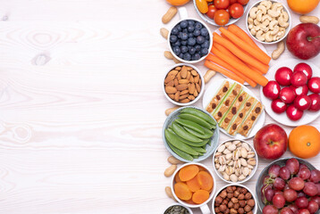 Healthy snacks such as fresh fruits, vegetables and nuts on white wooden table, top view with copy space