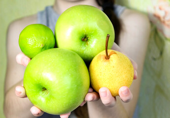 The girl holds apples, lime and a yellow pear in her hands.
