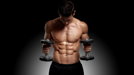 Front image of a fit, strong young man with bare torso, training with dumb-bell, showing six pack abs, black background.