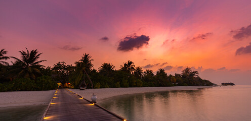 Sunset on Maldives island, luxury resort hotel and wooden pier jetty. Wonderful colorful sky clouds and beach sea horizon. Summer romantic vacation holiday, travel concept. Paradise sunset landscape