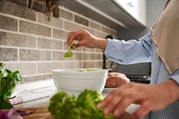 Closeup of woman tearing lettuce leaves with her hands and throws them into a bowl of vegetables to make healthy vegetable salad