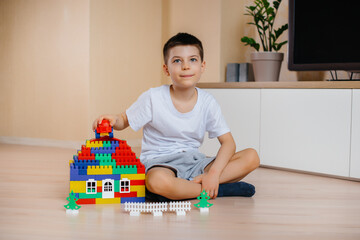 A little boy plays with a construction kit and builds a big house for the whole family. Construction of a family home.