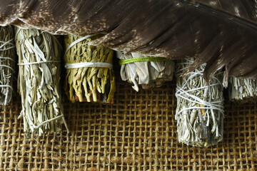 A top view image of a variety of healing smudge bundles with sacred feather on burlap. 