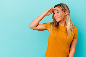 Young mixed race woman isolated on blue background looking far away keeping hand on forehead.