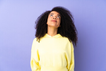 Young african american woman isolated on purple background and looking up