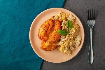 Baked chicken breast with salad on a plate decorated with spinach next to a fork on a concrete background on a blue napkin stand.
