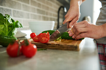 Close up of hands of a woman cutting vegetables and preparing raw vegan salad. Vegetables lying on a kitchen table