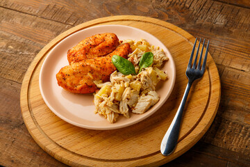 Baked chicken breast with salad with herbs on a plate next to a fork on a wooden table on a round stand.