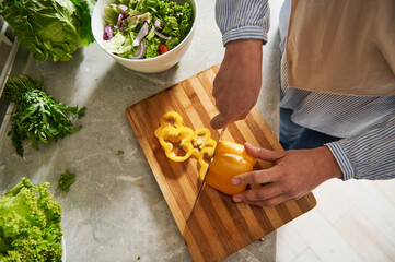 High angle view of female hands holding a knife and cutting yellow pepper into rings