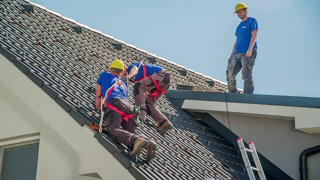Three Workers Readying Roof For Solar Panel Installation. Low Angle, Follow Shot Right
