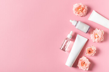 Obraz na płótnie Canvas Bottles of serum and cream tube with rose flowers flat lay on pink background