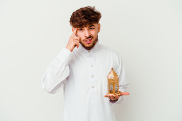 Young Moroccan man wearing a typical arab clothes holding a ramadan lamp isolated on white background showing a disappointment gesture with forefinger.