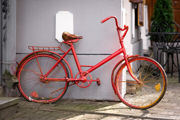 Fototapeta na wymiar Red retro bicycle parked outside cafe building against grey wall background. Bright, old, out of order, vintage womens bike with broken wheels. Transport in the summer. Close up