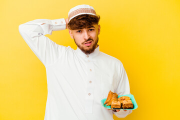 Young Moroccan man wearing the typical arabic costume eating Arabian sweets isolated on yellow background being shocked, she has remembered important meeting.