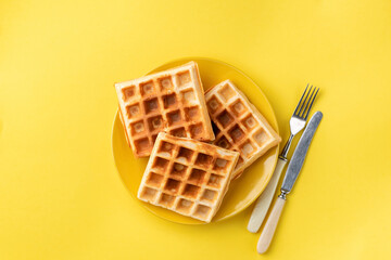 Belgian waffles on plate on yellow background. Isolated on yellow plate of sweet waffles
