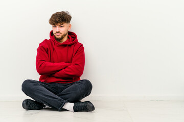 Young Moroccan man sitting on the floor isolated on white background suspicious, uncertain, examining you.
