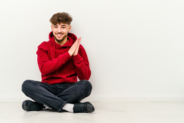 Young Moroccan man sitting on the floor isolated on white background feeling energetic and comfortable, rubbing hands confident.