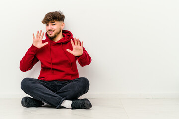 Young Moroccan man sitting on the floor isolated on white background rejecting someone showing a gesture of disgust.