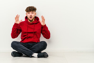 Young Moroccan man sitting on the floor isolated on white background celebrating a victory or success, he is surprised and shocked.