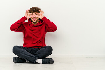 Young Moroccan man sitting on the floor isolated on white background keeping eyes opened to find a success opportunity.
