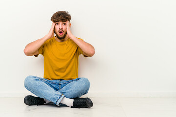 Young Moroccan man sitting on the floor isolated on white background being shocked, she has remembered important meeting.