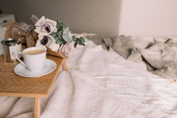 Fototapeta na wymiar Coffee table on bed. Flowers, coffee cup and candles. Interior gray tones, plaid