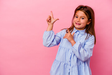 Little caucasian girl isolated on pink background  pointing with forefingers to a copy space,...