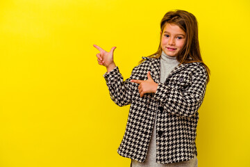 Little caucasian girl isolated on yellow background pointing with forefingers to a copy space, expressing excitement and desire.