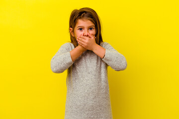 Little caucasian girl isolated on yellow background covering mouth with hands looking worried.