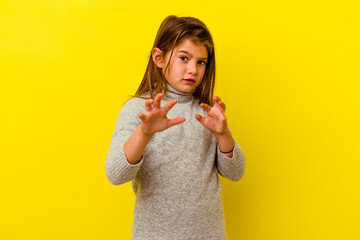 Little caucasian girl isolated on yellow background showing claws imitating a cat, aggressive gesture.