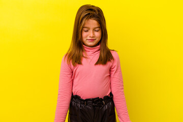 Little caucasian girl isolated on yellow background laughs and closes eyes, feels relaxed and happy.