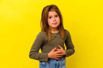 Little caucasian girl isolated on yellow background touches tummy, smiles gently, eating and...