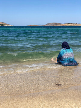 muslim woman sitting in the water on the sea shore with her clothes