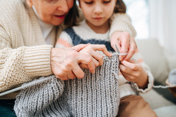 Enthusiastic granny tutoring her granddaughter, teaching her how to knit