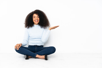 Young african american woman sitting on the floor holding copyspace imaginary on the palm to insert...