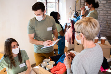 Group of volunteers with face mask working in community charity donation center.