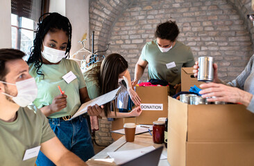 Group of volunteers with face mask working in community charity donation center.
