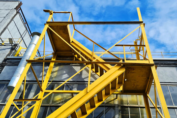 Big Yellow Staircase Near Industrial Plant Building on a Blue Sky Background.