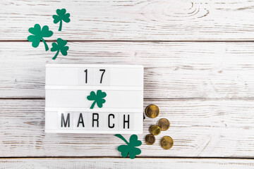 Flatlay for St. Patricks Day. Gold coins and shamrock clover leaves on a white wooden background....