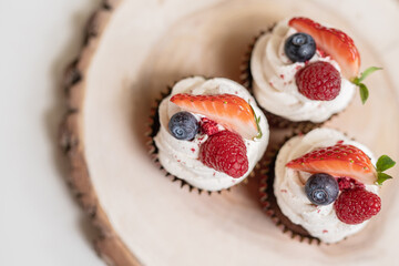 red cream cupcakes with strawberries and blueberries on natural wood coasters