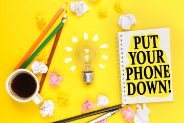 On a yellow background, a cup of coffee, a light bulb, pencils, a notebook with the inscription - PUT YOUR PHONE DOWN