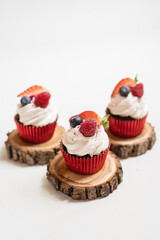 red cream cupcakes with strawberries and blueberries on natural wood coasters