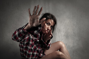 Fototapeta na wymiar Domestic violence or abuse concept: Frightened helpless woman making stop gesture with hand and trying to protect herself while looking at camera.