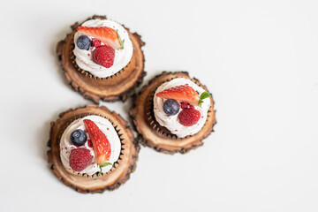 red cream cupcakes with strawberries and blueberries on natural wood coasters