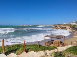 The path descends to a deserted sandy beach. Waves crash against the coastal sand.