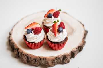 red cream cupcakes with strawberries and blueberries on natural wood coasters